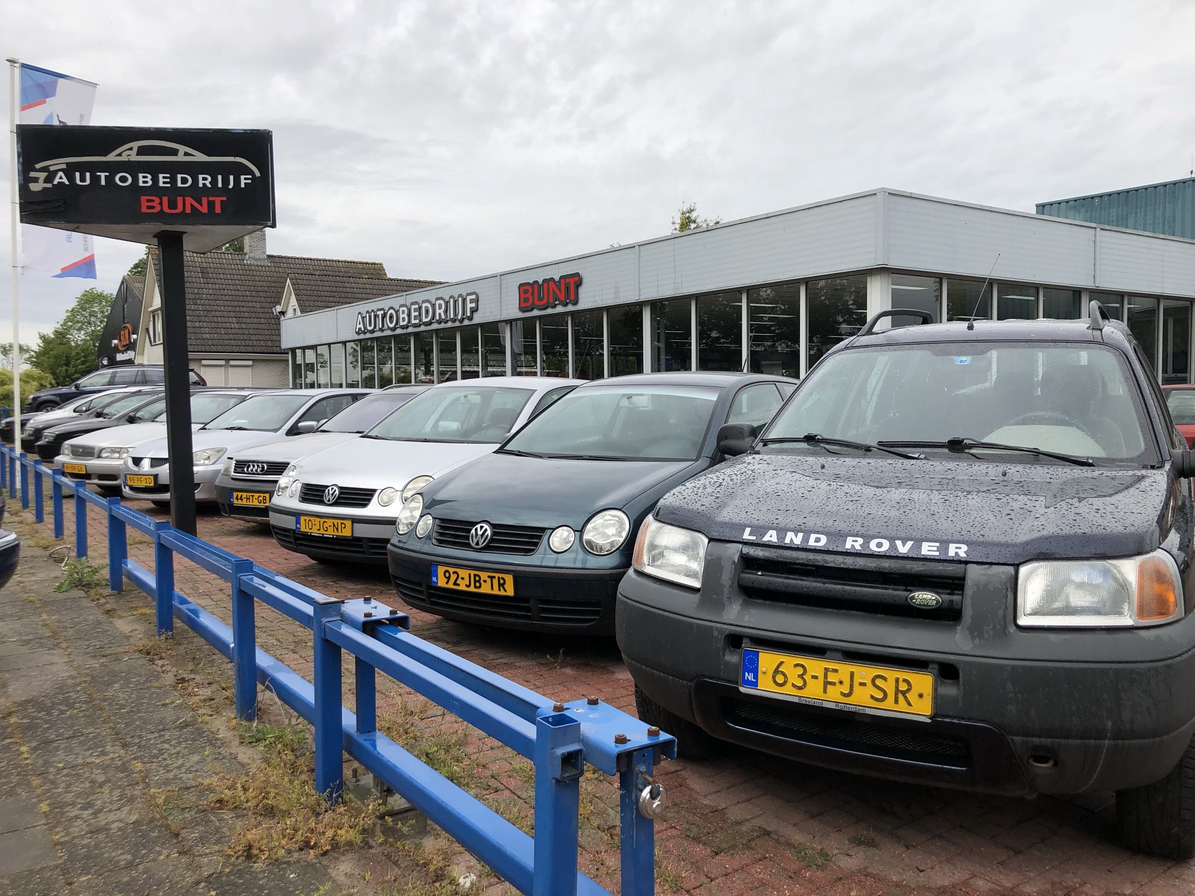 Het voorterrein met de reclamezuil, een Volkswagen Polo en een Land Rover Freelander