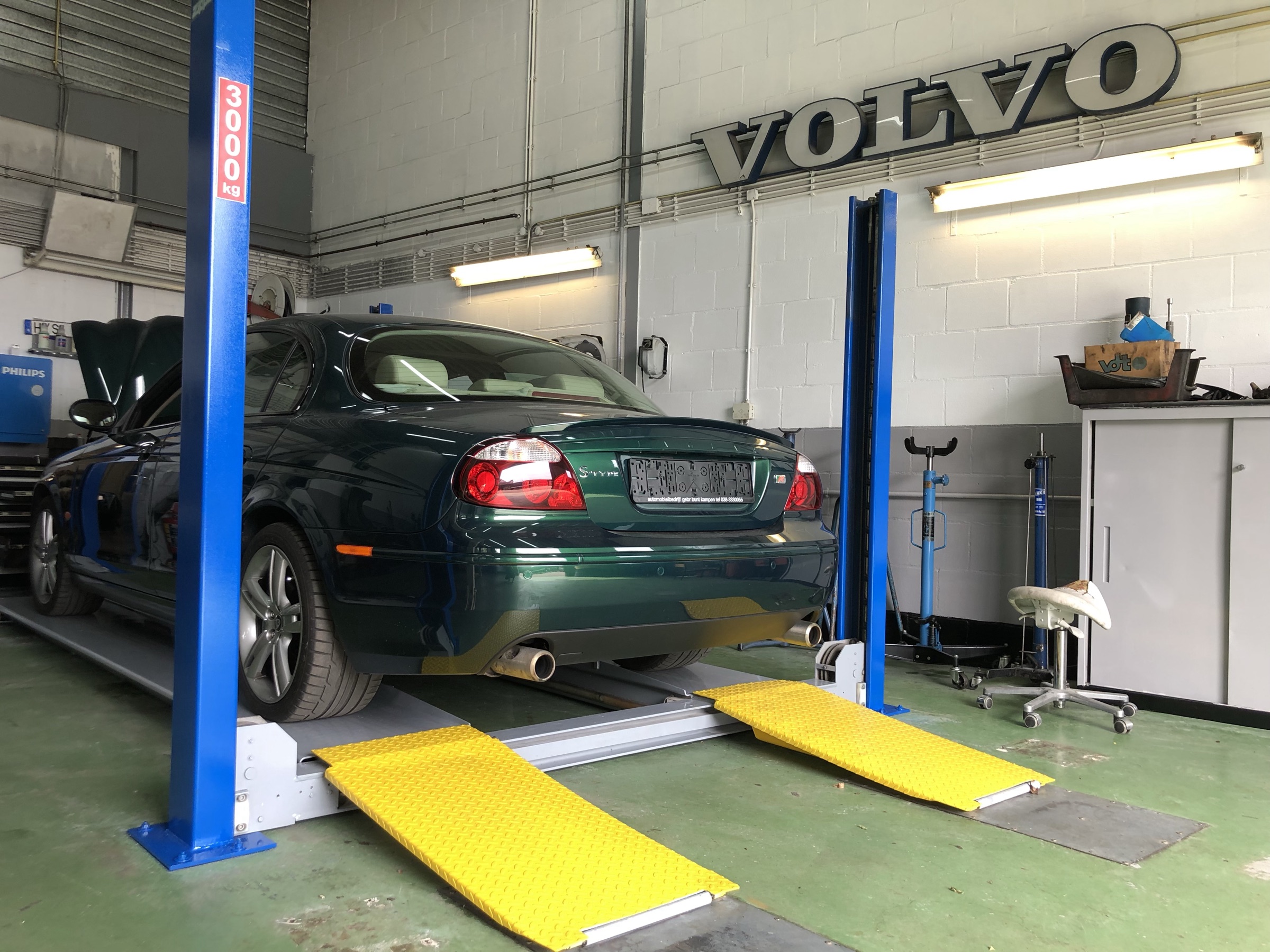 De werkplaats met de VOLVO-letters aan de muur en een groene Jaguar S-type op de brug